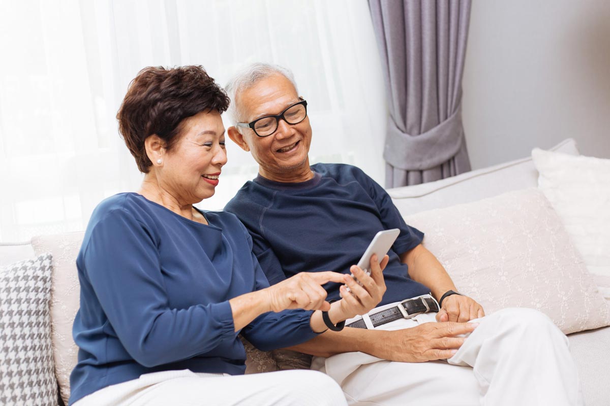 Senior Asian couple grandparents using a smart phone together on sofa at home