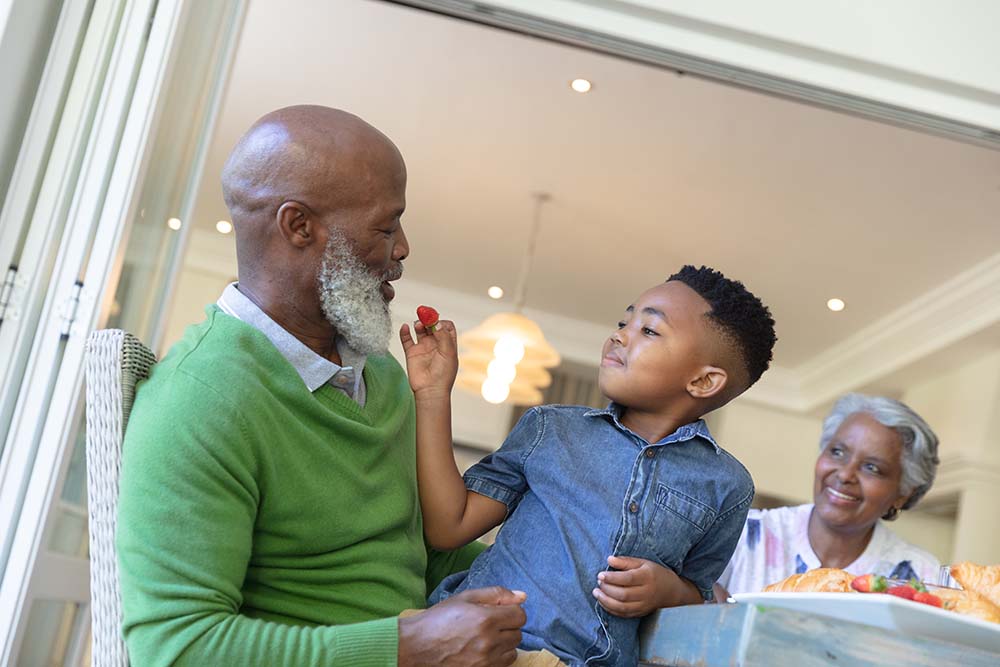 Happy african american grandson and grandparents sitting at tabl